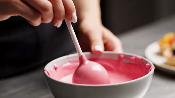Hand dipping a cake pop in pink candy coating